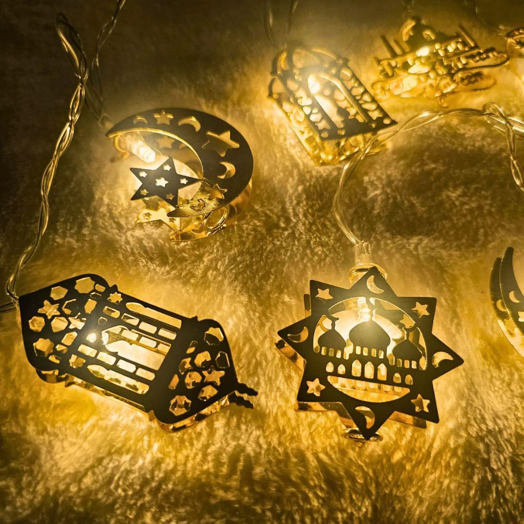 Close-up of golden Ramadan and Eid metal string lights with crescent moon, mosque, and lantern designs glowing warmly by Islamify