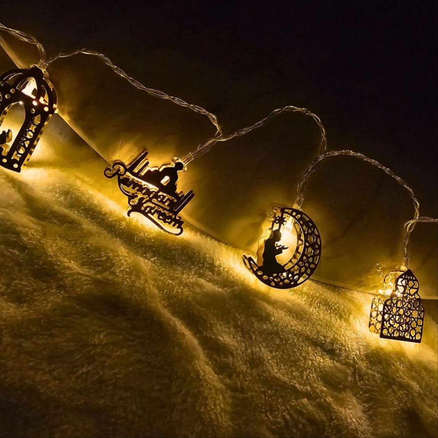 Warm golden Ramadan and Eid string lights featuring lantern, mosque, and crescent moon designs illuminating a soft fabric surface by Islamify