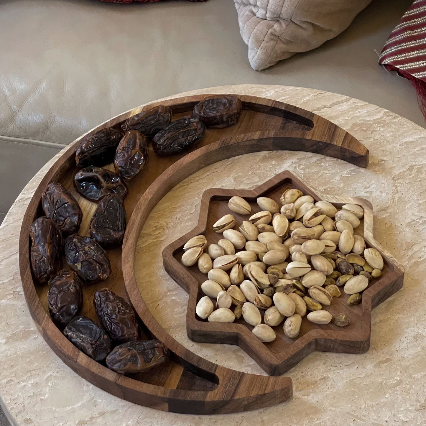 A crescent-shaped wooden plate filled with dates next to a star-shaped wooden plate filled with pistachios, placed on a table – Islamify Ramadan decor