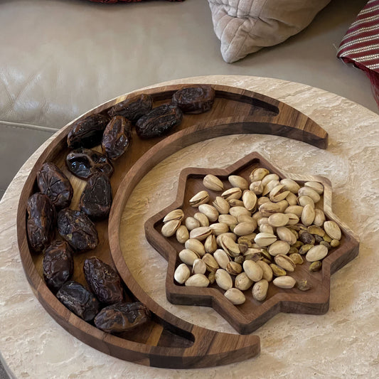 A crescent-shaped wooden plate filled with dates next to a star-shaped wooden plate filled with pistachios, placed on a table – Islamify Ramadan decor